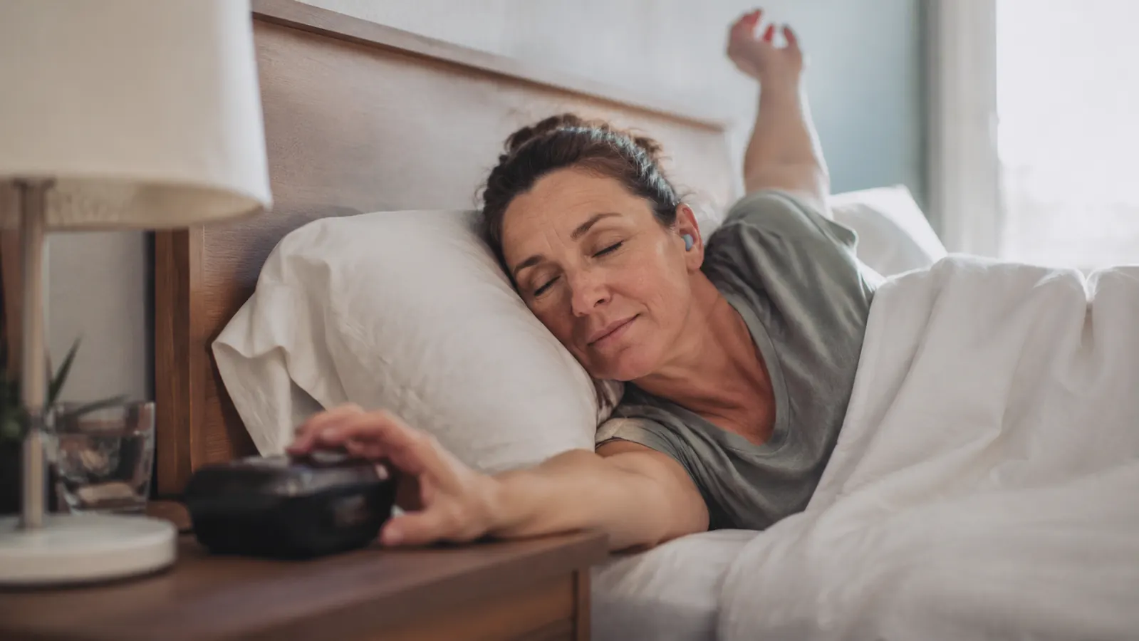 Person waking up to a vibrating alarm clock on the nightstand with earplugs still in